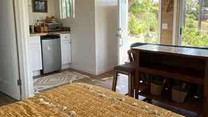 Une pièce comprenant un lit, une table à manger, un coin cuisine et donnant sur l’extérieur.