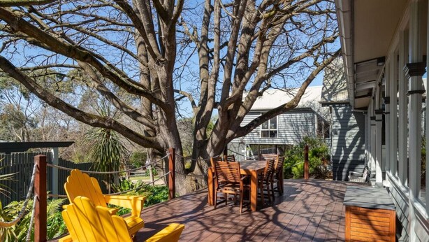 A wooden deck with a table and chairs, surrounded by trees and a house.