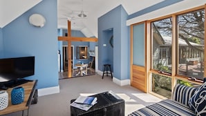A modern living room with a large TV, a dining area, and a view of the outdoors.