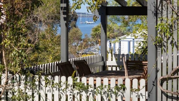 A garden with a pergola, white picket fence, and a view of a body of water.