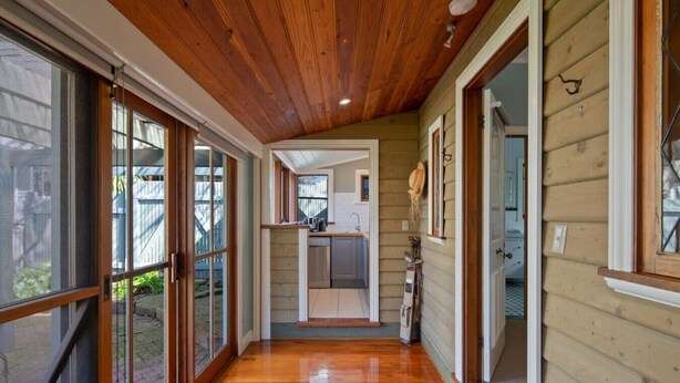 Un pasillo con suelo de madera y ventanas amplias, que conduce a una zona de cocina con fregadero y armarios.