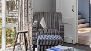 Ein modernes Wohnzimmer mit einem gestreiften Sessel, einem Glastisch und Blick auf eine Treppe.
