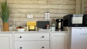 A kitchen with white cabinets, a microwave, a coffee maker, and a small plant on the counter. - Adorable Cabin in the Countryside (Mountrath)