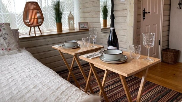 A cozy room with a bed, a dining table set with plates and glasses, a chair, and a bottle of wine. - Adorable Cabin in the Countryside (Mountrath)