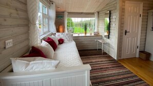 A cozy room with a white sofa, a small table, and a window with a view of greenery. - Adorable Cabin in the Countryside (Mountrath)