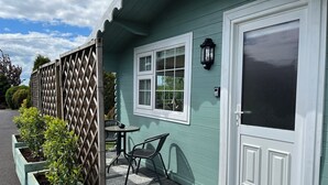 A house with a front door, a window, a porch with a table and chairs, and a lattice fence. - Adorable Cabin in the Countryside (Mountrath)