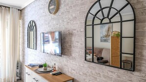 Une pièce avec un mur en briques, un meuble en bois doté de tiroirs, un téléviseur à écran plat et deux miroirs fixés au mur.