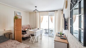 Un espace de vie compact comprenant un lit, un coin repas, une petite cuisine et un balcon.