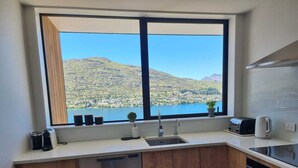 A kitchen with a large window, stainless steel appliances, and a view of a lake and mountains. - Vues on Angelo | 3BR Home, Lake & Remarkables View (Queenstown)