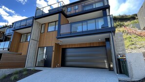 A modern two-story house with a garage, large windows, and a balcony. - Vues on Angelo | 3BR Home, Lake & Remarkables View (Queenstown)