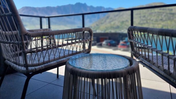 A balcony with wicker chairs and a glass table, overlooking a mountainous landscape and a body of water. - Vues on Angelo | 3BR Home, Lake & Remarkables View (Queenstown)