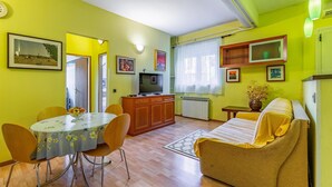 Een woonkamer met een bank, een eettafel met stoelen, een televisie en een radiator.
