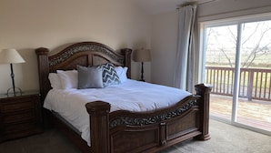 A large bed with a wooden headboard, two bedside tables with lamps, and a view of a deck through a sliding glass door. - Montana ranch house sunrise sunset views & fields (Bozeman)