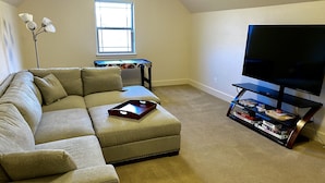 A living room with a sectional sofa, a coffee table, a television, and a bookshelf. - Montana ranch house sunrise sunset views & fields (Bozeman)