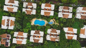 An aerial view of a resort with multiple bungalow-style buildings, a central swimming pool, and lush tropical vegetation. - CONDO BELLA BY TRVL2HM (Puerto Vallarta)