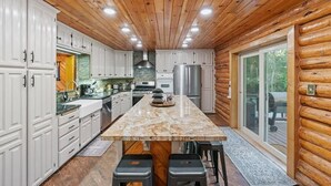 A log cabin kitchen with white cabinets, a marble island, and a large window. - Private Island, FirePit, HotTub, Arcade, AC, Dogs! (Rigby)
