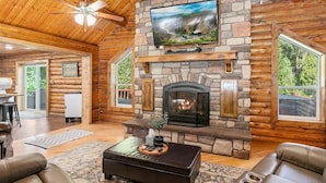A log cabin interior with a stone fireplace, a mounted TV, and leather seating. - Private Island, FirePit, HotTub, Arcade, AC, Dogs! (Rigby)
