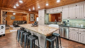 A spacious kitchen with a large island, white cabinets, and a stone backsplash. - Private Island, FirePit, HotTub, Arcade, AC, Dogs! (Rigby)