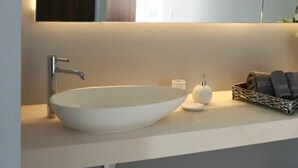 A modern bathroom with a large white sink, a mirror, and a dark wooden panel above the mirror. - CONDO 57 BY TRVL2HM (Puerto Vallarta)