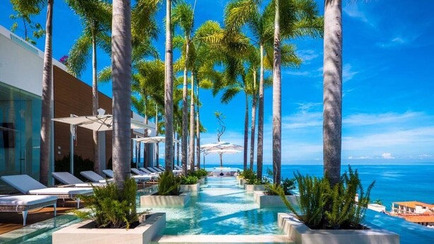 A pool area with lounge chairs and palm trees, leading to a view of the ocean. - CONDO 57 BY TRVL2HM (Puerto Vallarta)
