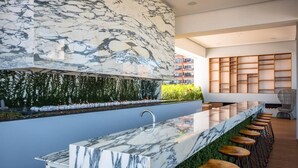A modern bar area with a marble countertop, wooden stools, and a green wall with plants. - CONDO 57 BY TRVL2HM (Puerto Vallarta)