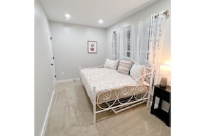 Cozy retreat with a single bed, bedside table, and window with sheer curtains.
