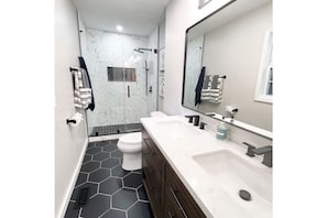 Features a walk-in shower, glass door, and hexagonal tile floor.