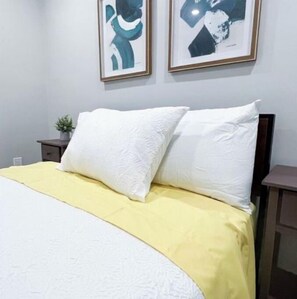 Cozy retreat with a neatly made bed, framed artwork, and a bedside table.