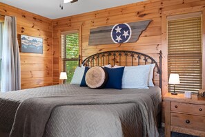 Quarto de cabana de madeira com cama, duas luminárias de apoio, mesa de cabeceira e um adorno na parede.