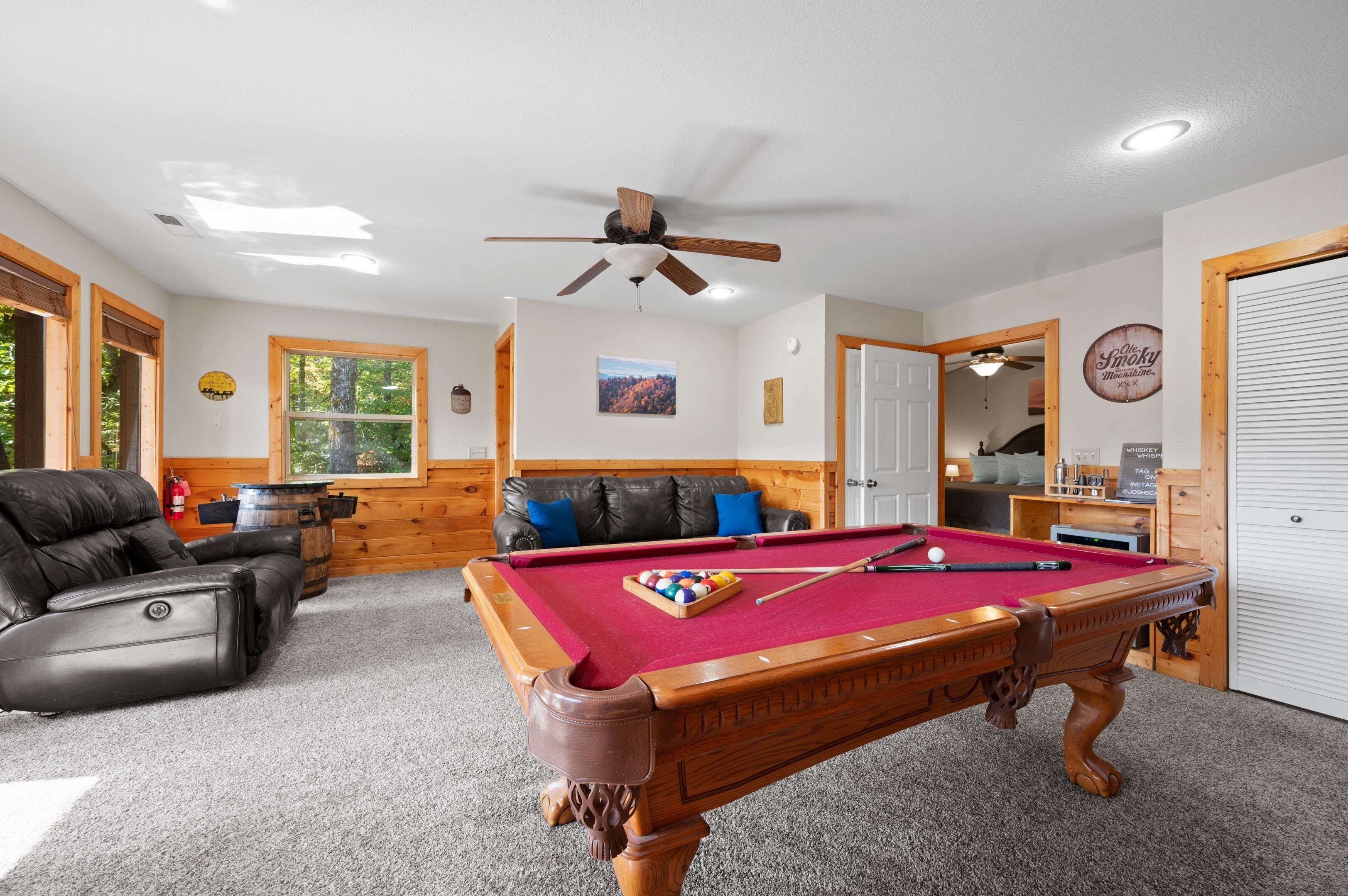 A pool table in a room with a ceiling fan, a leather couch, and a fireplace.