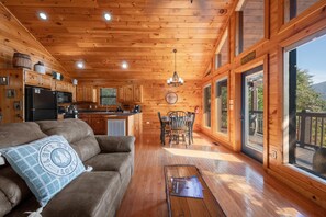 L’intérieur d’un chalet en bois comprend une cuisine, un coin repas et une grande fenêtre donnant sur une terrasse.