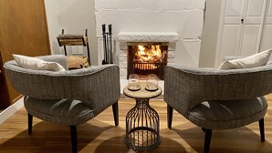 Un rincón acogedor con dos sillones grises, una mesita de madera y una chimenea encendida.