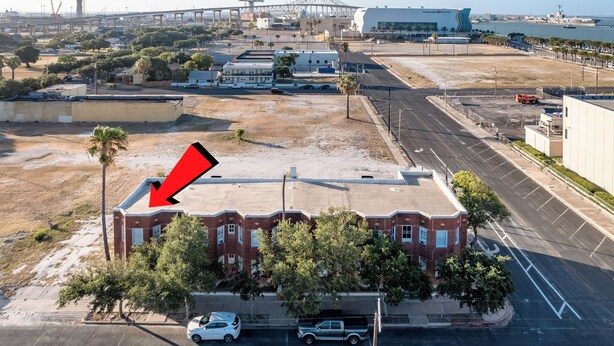 Vue aérienne d’une zone côtière, avec un bâtiment imposant doté d’un toit rouge, un pont en arrière-plan et une étendue d’eau.