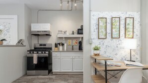 A compact kitchen with white cabinets, a stainless steel stove, and a wooden dining table with a white chair.