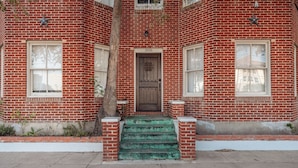 A red brick building with a wooden door, numbered 306, and a small tree in front.