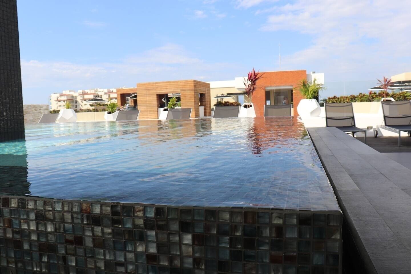 A modern hotel pool area with a clear view of the pool, lounge chairs, and a building with a glass facade.