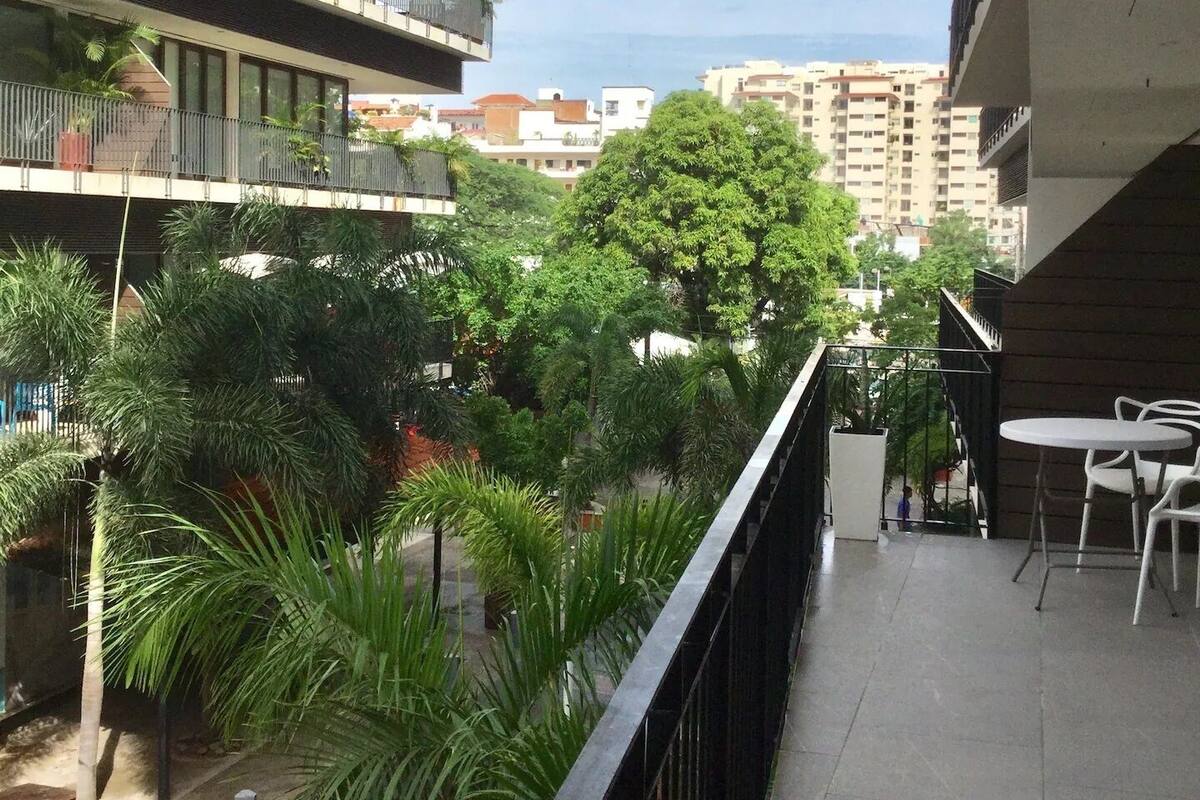 A balcony with a view of a green courtyard, a tree, and a building in the background.