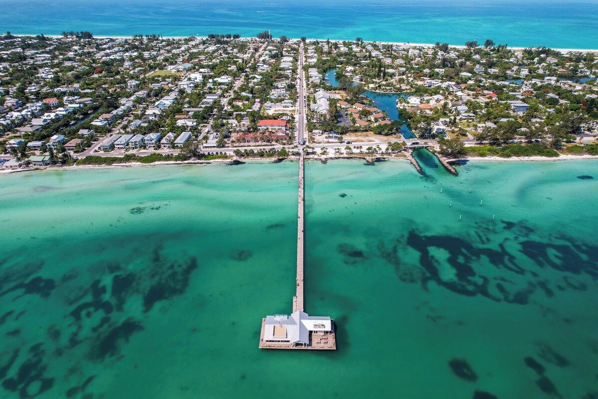 An aerial view of a coastal area with a long pier extending into the turquoise waters.