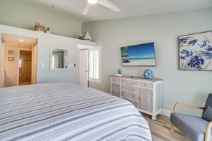 A bedroom with a large bed, a dresser, a chair, a painting of a beach scene, and a mirror.