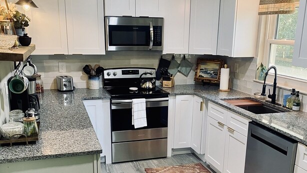 A modern kitchen with white cabinets, stainless steel appliances, and a granite countertop. - Private Retreat with your dogs: close to WEC (Ocala)