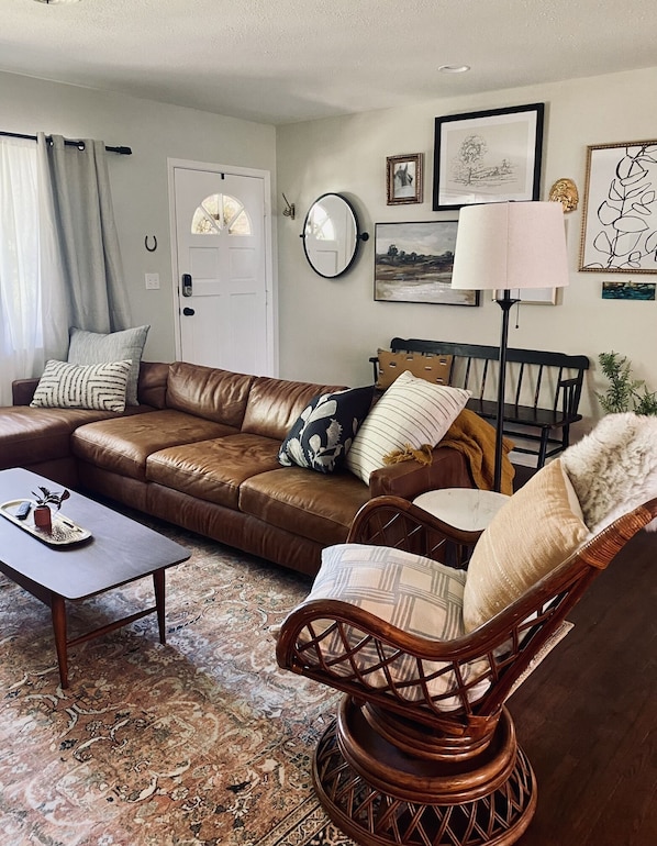 A living room with a brown leather sofa, a wooden chair, a coffee table, and a patterned rug.