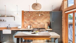 Une cuisine moderne avec un mur en briques, des armoires en bois, un îlot central et des luminaires suspendus.
