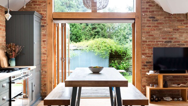 Une cuisine moderne avec une grande table à manger, un plancher en bois et un téléviseur fixé à un mur en briques.