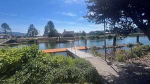 A lakeside view with a wooden dock, a stone pathway, and a grassy area with bushes.