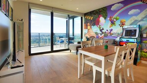 A spacious room with a large sliding glass door leading to a balcony, a Nintendo 64 gaming console, and a mural with animated characters.