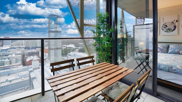 A balcony with a wooden table and chairs, a potted plant, and a bed with floral bedding.