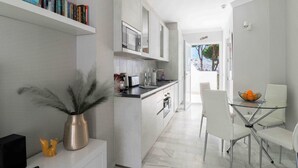 Una cucina moderna con mobili bianchi, forno a microonde integrato e zona pranzo con tavolo in vetro e sedie bianche.