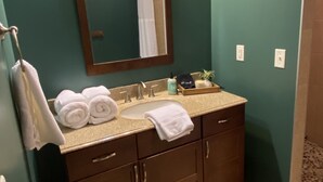 A bathroom with a dark teal wall, a wooden vanity with a sink, and a mirror above it. There are towels on the vanity and a shower curtain visible in the mirror. - Quiet rural home located 2 miles from downtown Milford (Milford)