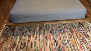 A neatly made bed with a grey mattress and patterned pillows, flanked by two bedside tables with lamps, a framed quote on the wall, and a colorful woven rug on the floor. - Quiet rural home located 2 miles from downtown Milford (Milford)