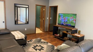 A modern living room with a leather sofa, a TV displaying a sports game, and a wooden entertainment unit. - Quiet rural home located 2 miles from downtown Milford (Milford)